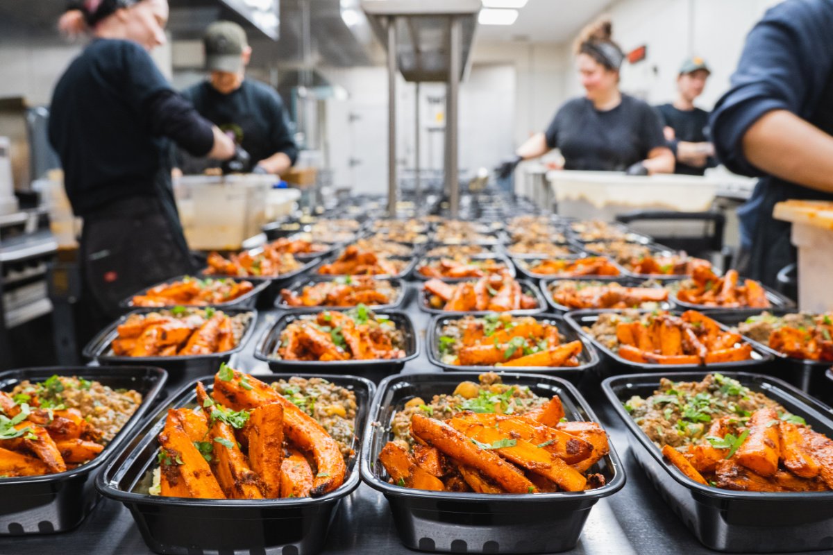 rows of to-go boxes of freshly made food, with chefs and cooks in the background