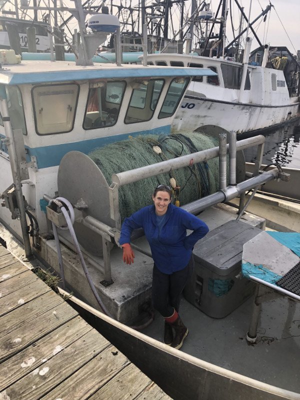 A fisher woman stands in her boat with her hands on her hips