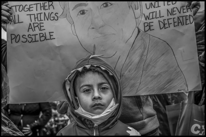 Top: Cesar Vasquez shouts out his poem to the crowd of marchers on March 30. Center: Two young women listen to Vasquez speak at the march. Bottom: At the march, a boy from a Mixteco (Mexican Indigenous) farmworker family with a hand-drawn portrait of Cesar Chavez. (Photos credit: David Bacon)